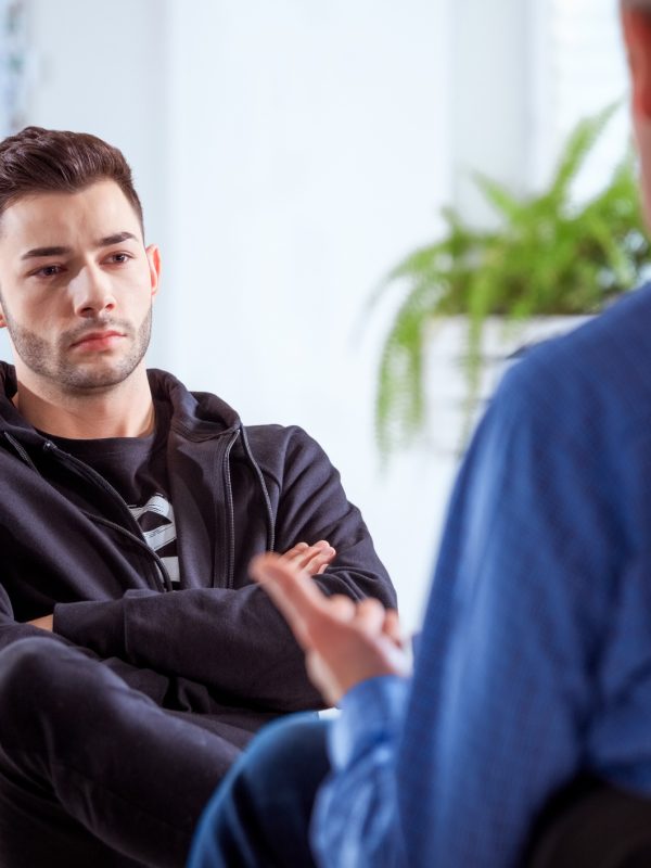 Serious student listening to therapist. Mature professional advising young man during session. They are sitting in meeting at lecture hall.