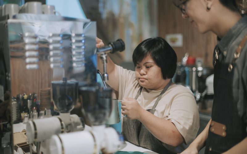 asian down syndrome female learning from barista making coffee in her café place of work